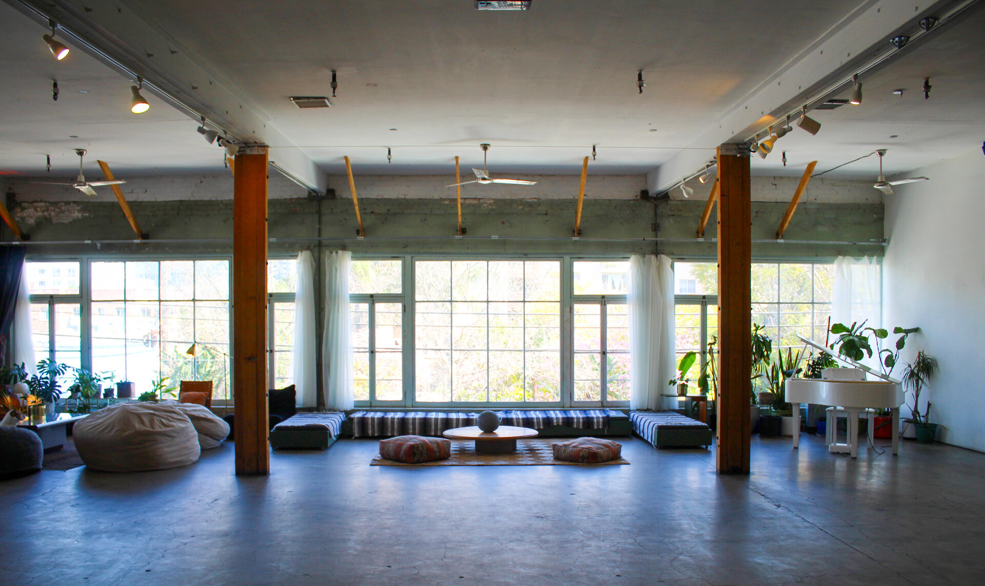 Studio A, the Loft, in daylight: an open concrete floor, wood columns and a full wall of windows