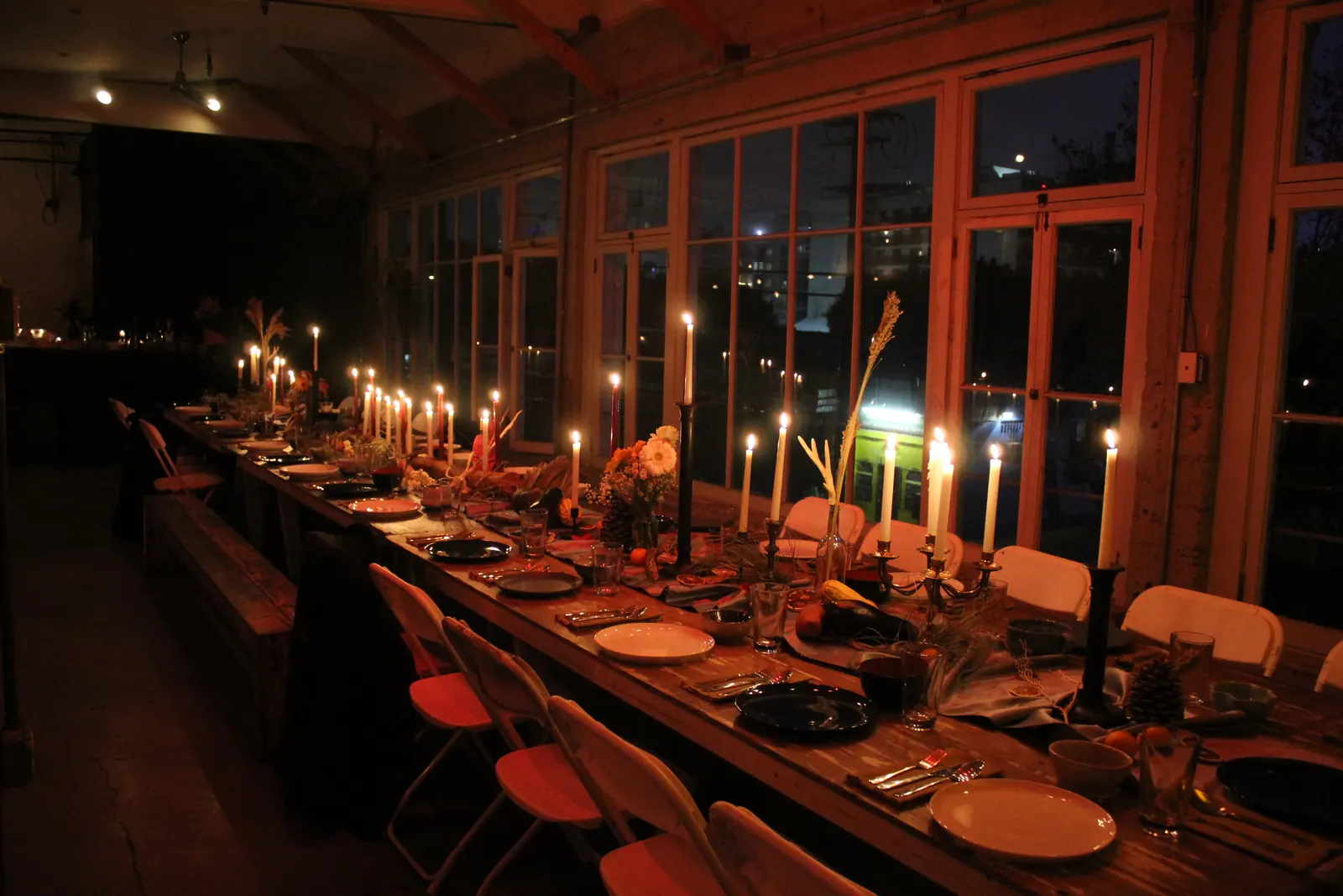 A long table set for dinner and lit by taper candles, beside the Loft windows at night